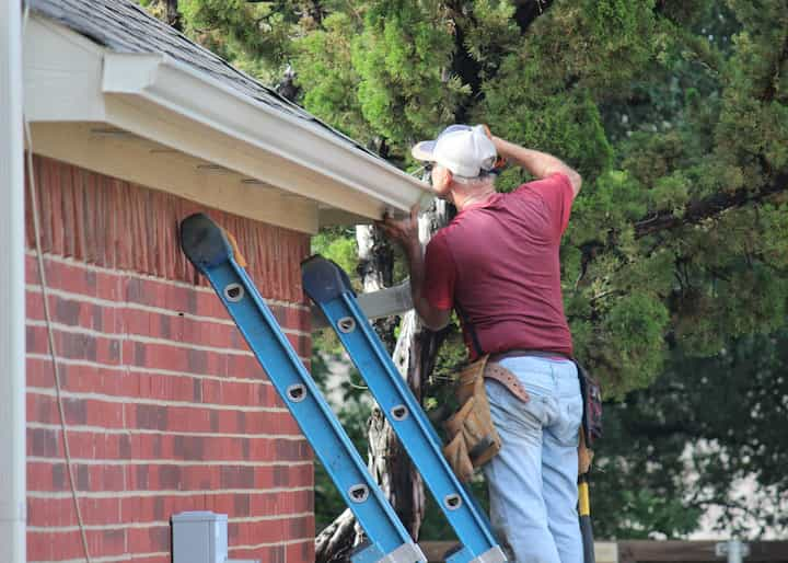 A roofing replacement expert on industrial ladder fixing gutters in Hot Springs, Arkansas